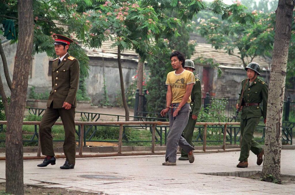 Um homem algemado é conduzido por soldados chineses em uma rua de Pequim, em junho de 1989, enquanto policiais e soldados procuravam pessoas envolvidas nos protestos pró-democracia de abril a junho.