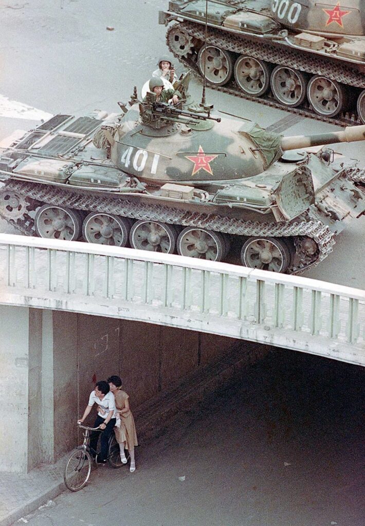 Um casal chinês em uma bicicleta se abriga sob uma passagem subterrânea enquanto tanques são enviados para cima no leste de Pequim, em 5 de junho de 1989.