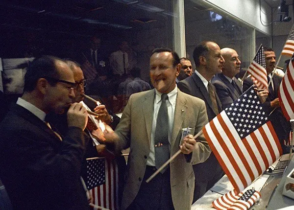 O Controle da Missão comemora com charutos e bandeiras americanas após o primeiro pouso bem-sucedido na Lua em 1969.