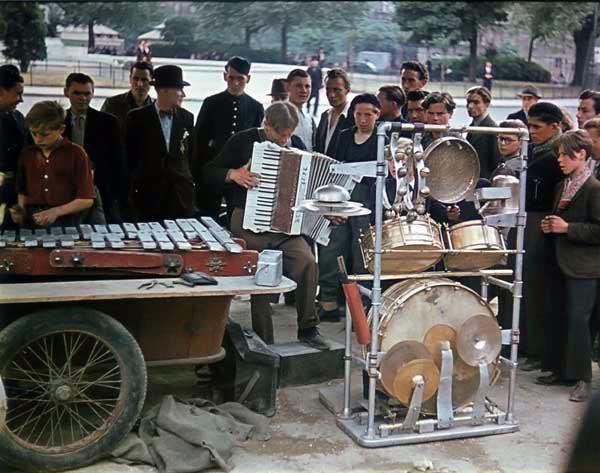 Uma multidão cerca uma banda itinerante enquanto eles tocam em uma rua de Paris.