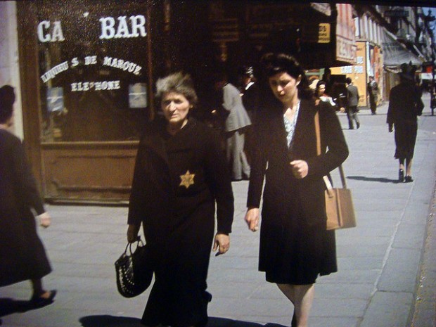 Uma senhora idosa caminha pela rua usando a estrela amarela que os nazistas forçaram os judeus a usar.