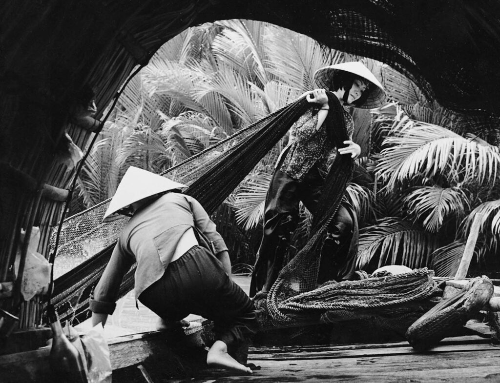 Mulheres puxam pesadas redes de pesca no braço superior do Rio Mekong, assumindo uma tarefa normalmente realizada exclusivamente por homens. 1974. (Foto de Le Minh Truong).