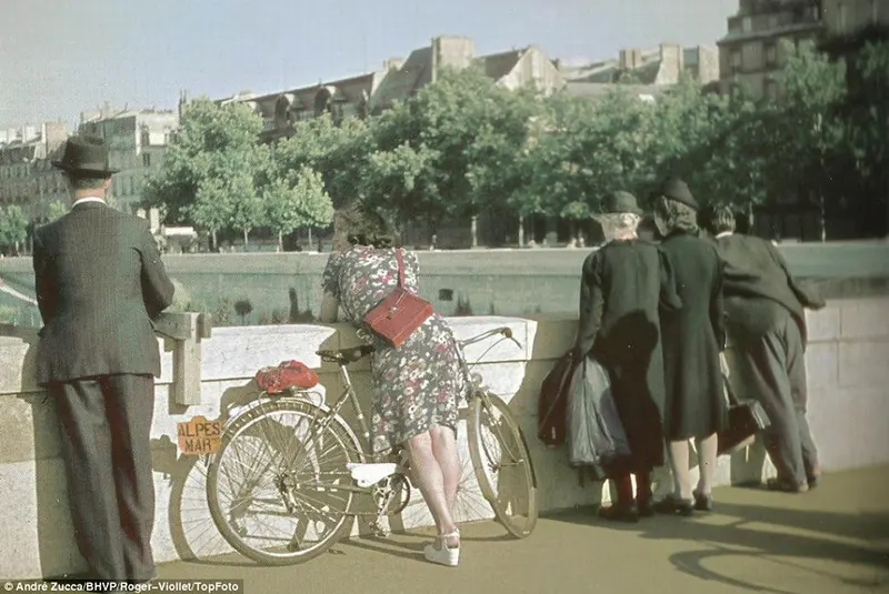 Uma mulher inclinada sobre a lateral da ponte é o foco desta fotografia.