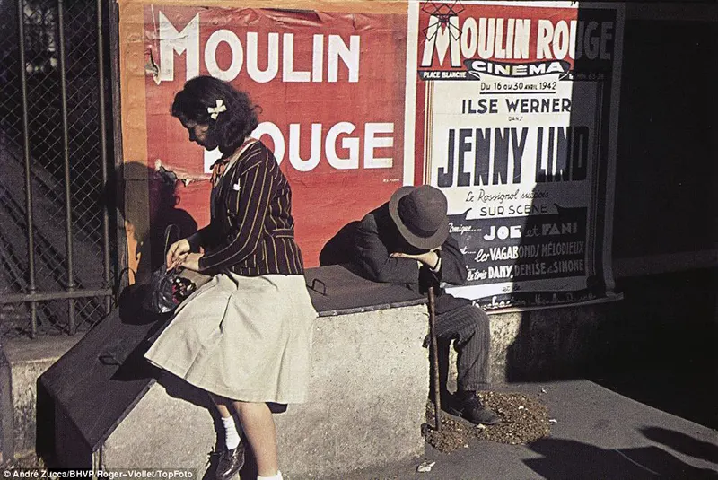 Uma jovem verifica sua bolsa enquanto um homem está sentado curvado sobre uma bengala em frente a cartazes do famoso cabaré Moulin Rouge da cidade.