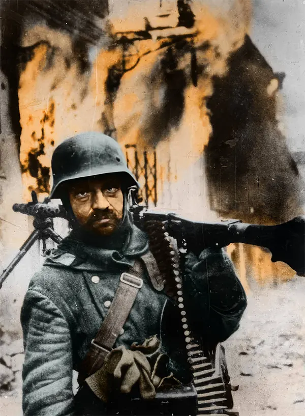 Um granadeiro alemão carregando uma metralhadora no ombro em frente a um prédio em chamas durante a retirada alemã na União Soviética, 1944.